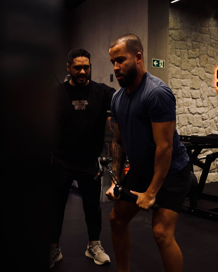 Professor da Silva Gym orientando um aluno no aparelho de cabo